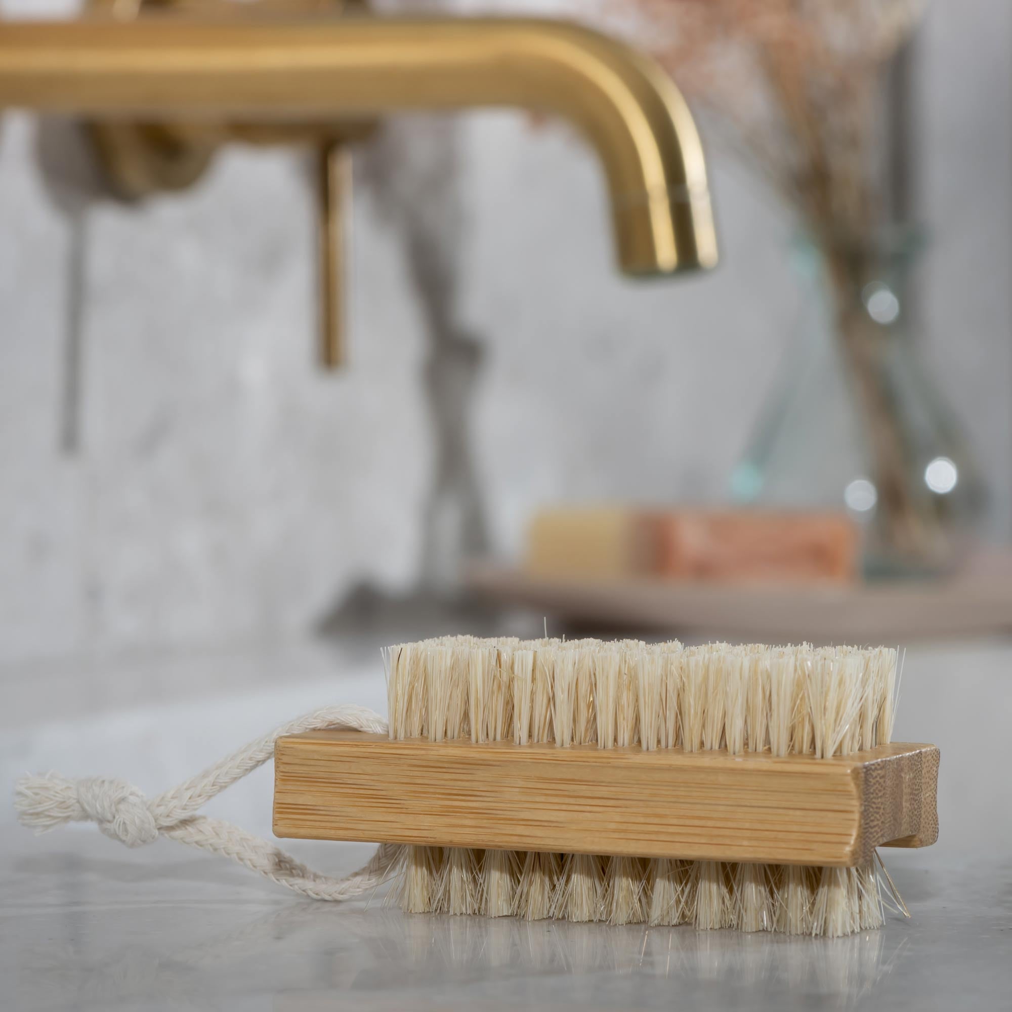 Bath brush with natural bristles on a bathroom counter with a blurred background. Victoria James Body Nail Brush