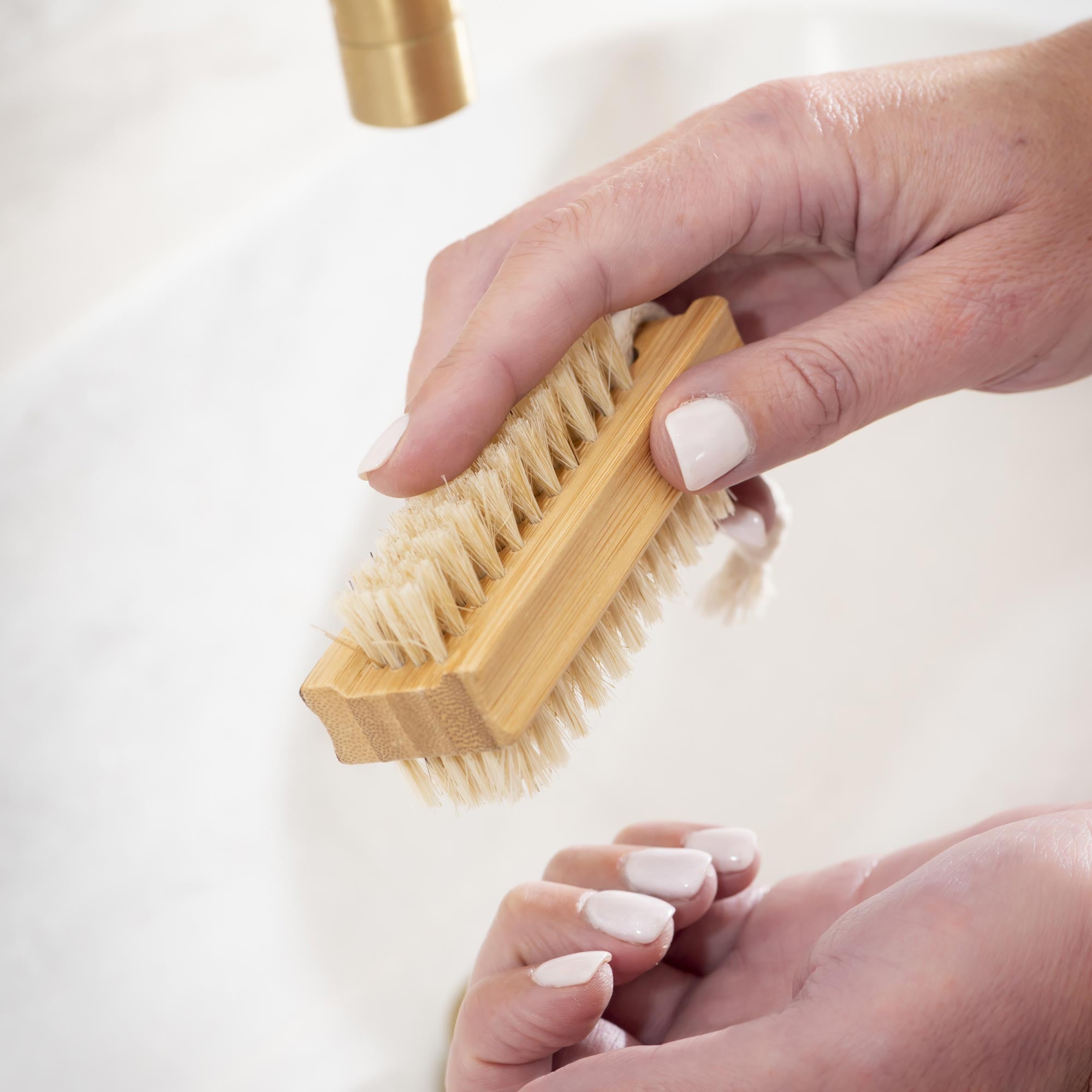 Hand holding a wooden nail brush with a white background. Victoria James Body Nail Brush