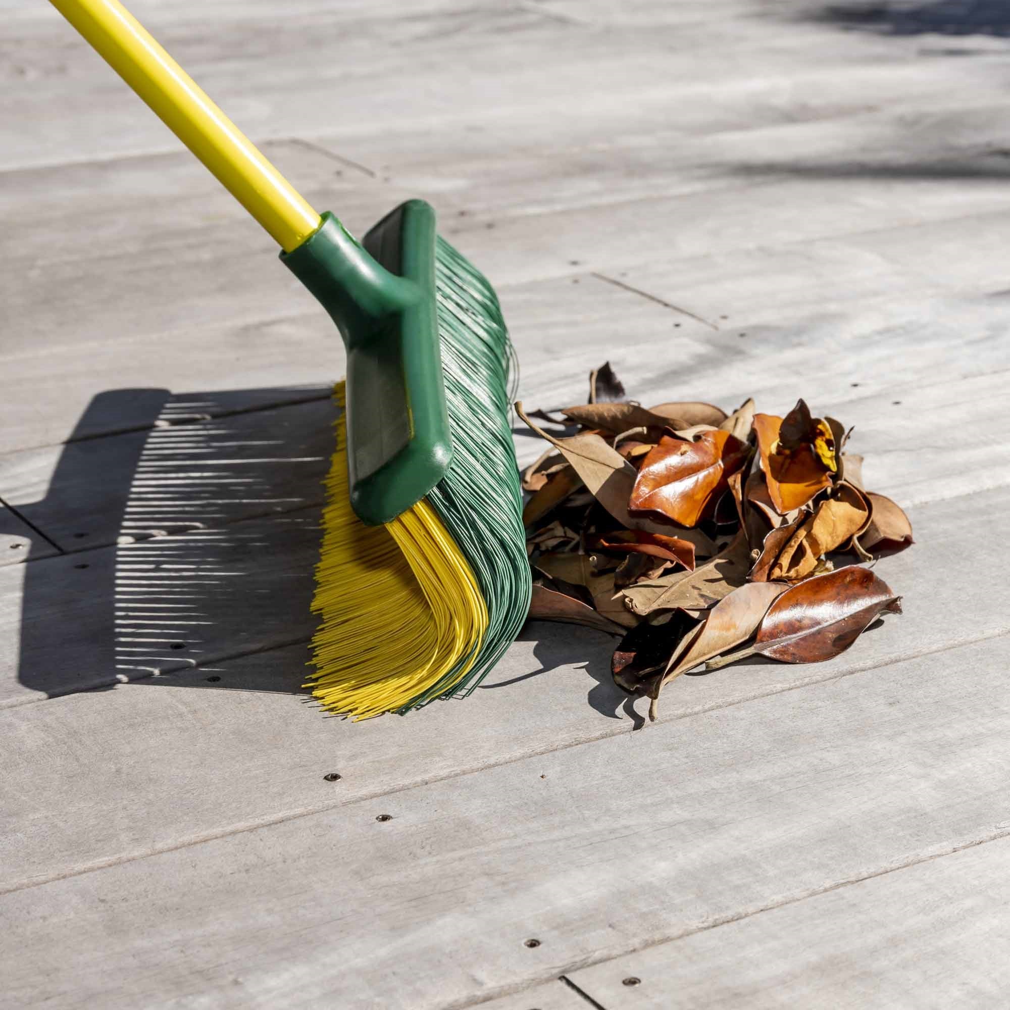 Green and yellow broom with a pile of leaves on a wooden deck. Simply Clean 2IN1 Broom & Rake