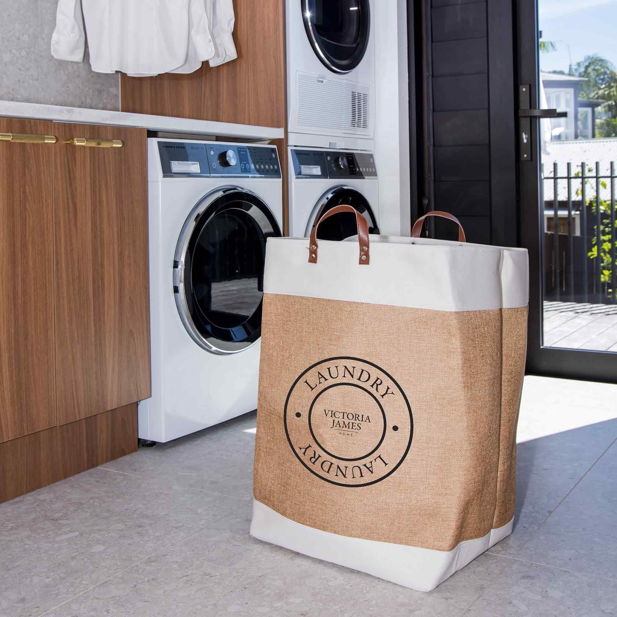 Laundry bag with 'Victoria James' branding in a laundry room setting. Victoria James Home Laundry Hamper