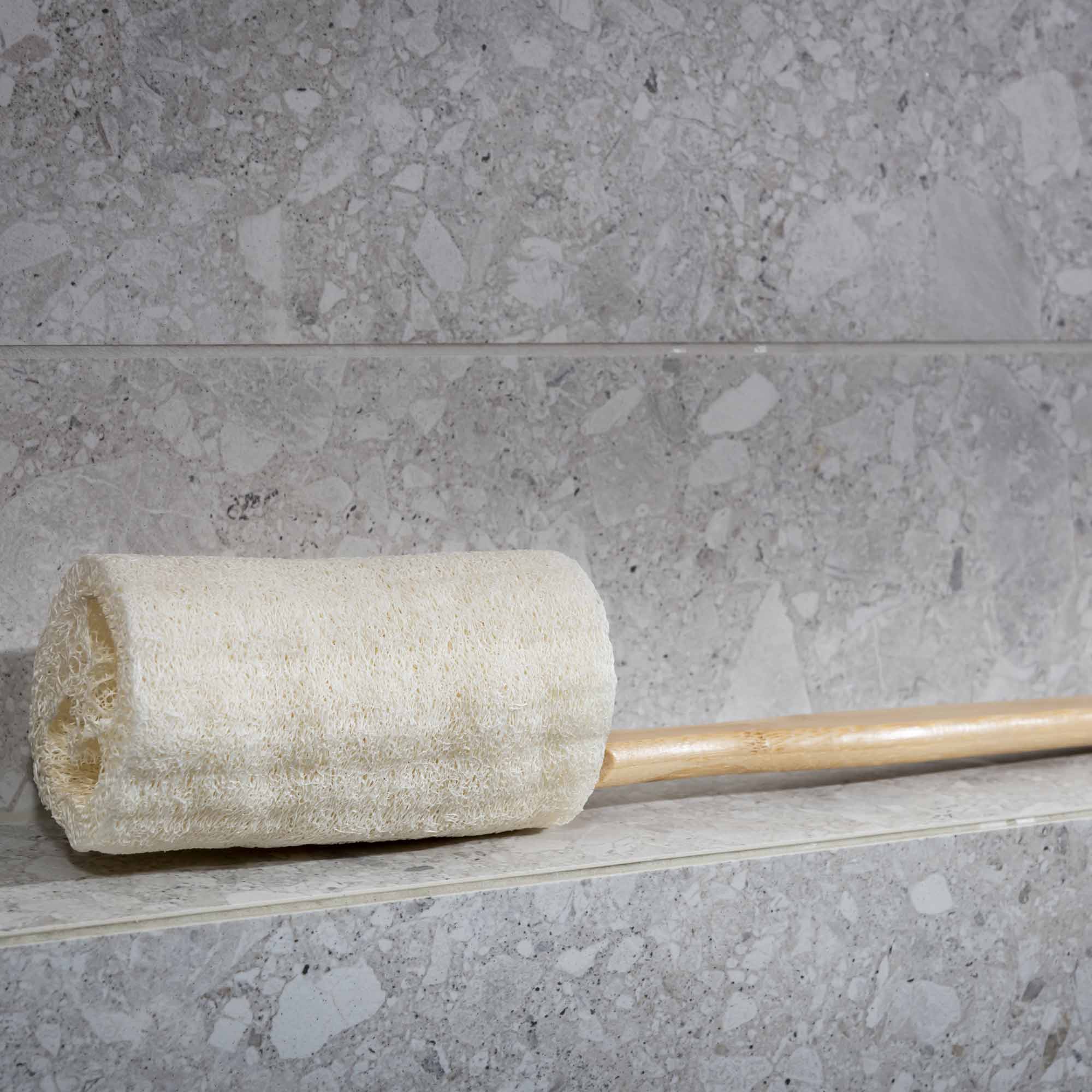 Roller with a beige cushion on a gray tiled floor. Victoria James Body Loofah Brush