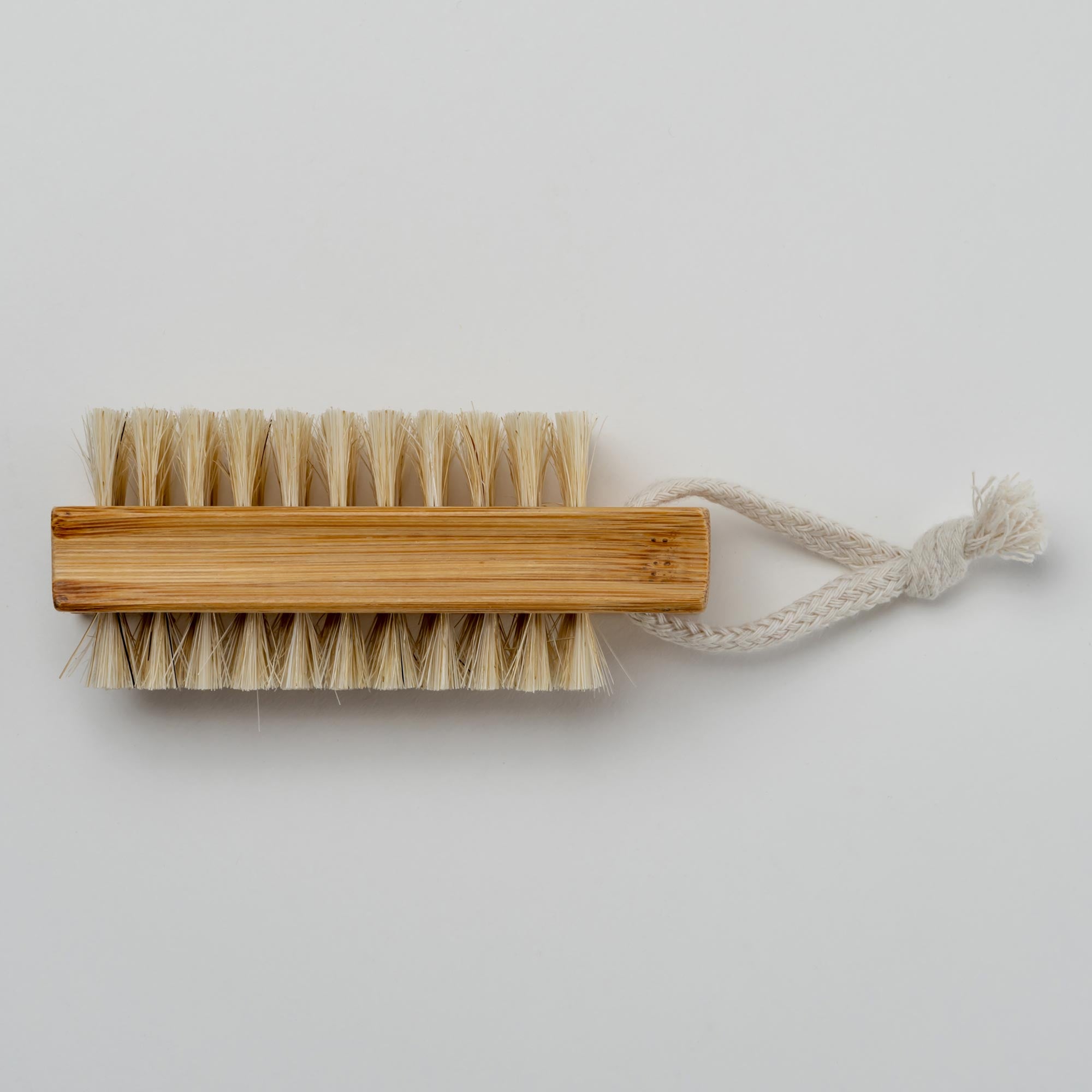 Bristle brush with wooden handle and rope on a light gray background. Victoria James Body Nail Brush