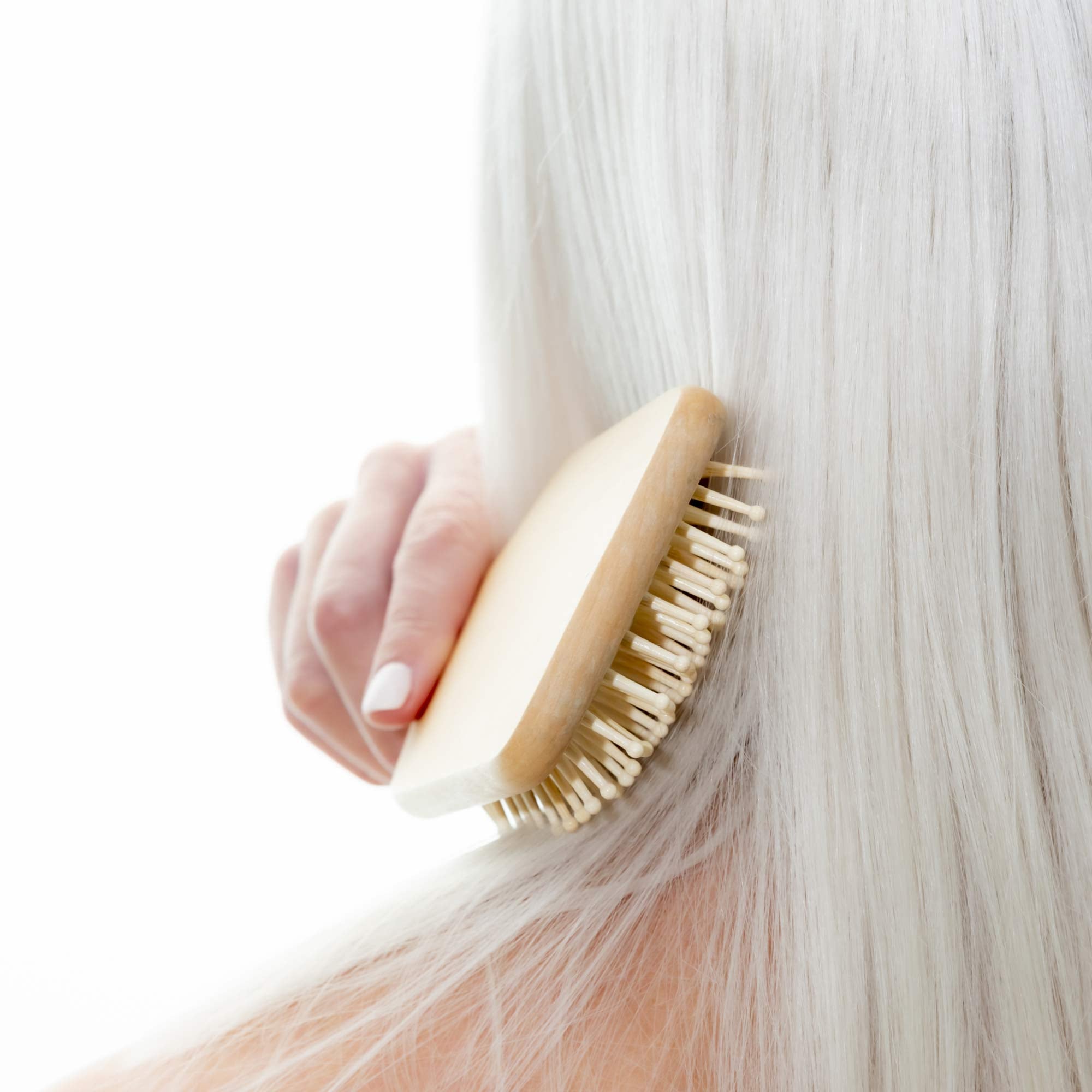 Person using a wooden hairbrush on their blonde hair against a white background. Victoria James Wooden Paddle Hair Brush